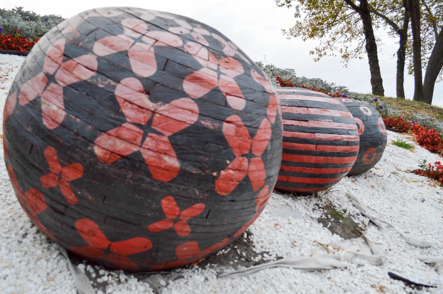 three large wooden black and red balls with patterns on white pebbles in the park photo