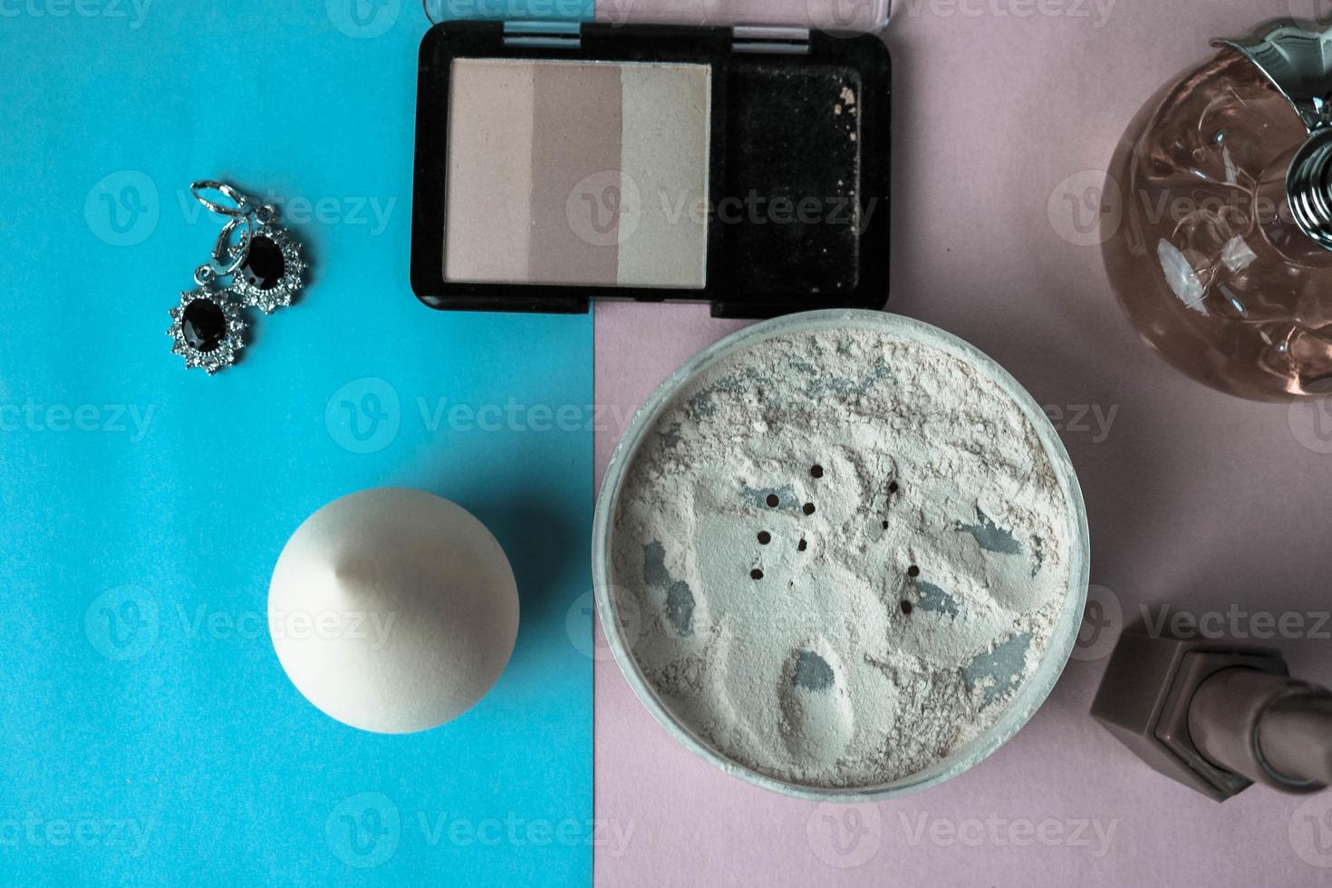 Beauty box, makeup kit, powder and blush with beauty blender, perfume, lipstick, highlighter and earrings for make-up on white and blue background. Flat lay. Top view photo