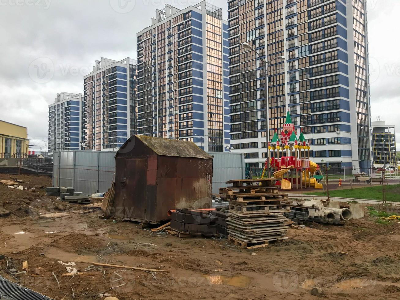 un pequeño garaje oxidado se encuentra en el centro de un nuevo complejo residencial. la casa oxidada se alza contra el telón de fondo de los altos edificios de apartamentos de cristal azul y blanco. paisaje urbano foto