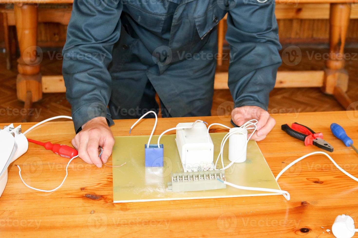 A man working electrician works, collects the electric circuit of a large white street lamp with wires, a relay at an industrial plant factory photo