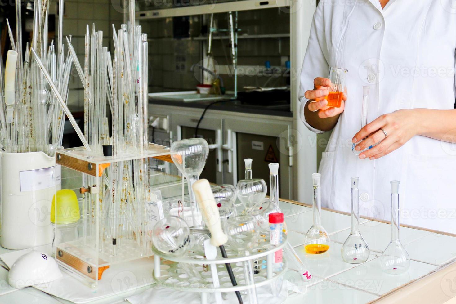 A female laboratory assistant, a doctor, a chemist, works with flasks, test tubes, makes solutions, medicines, mixes the ingredients in the laboratory. Laboratory assistant carries out the research photo