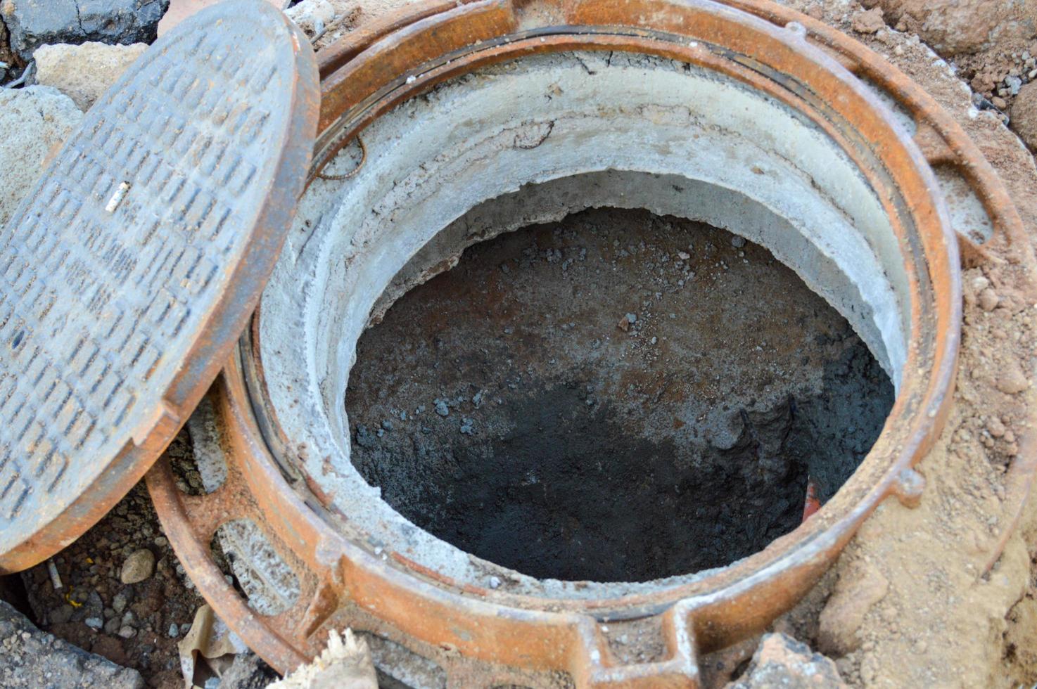 alcantarillado abierto en la calle. Túnel de metal para drenaje de agua, creando un pasaje de alcantarillado. tapa de alcantarilla oxidada, agujero de construcción. alcantarillado en el sitio de construcción. producción de un nuevo complejo residencial foto