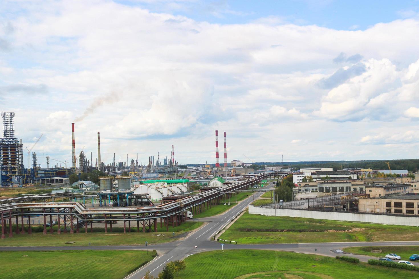 paisaje industrial. vista panorámica de las tuberías tecnológicas. ajustes de la planta. de las tuberías químicas rojo-blancas sale humo. edificios de producción. contra el fondo del cielo y la hierba brillante foto