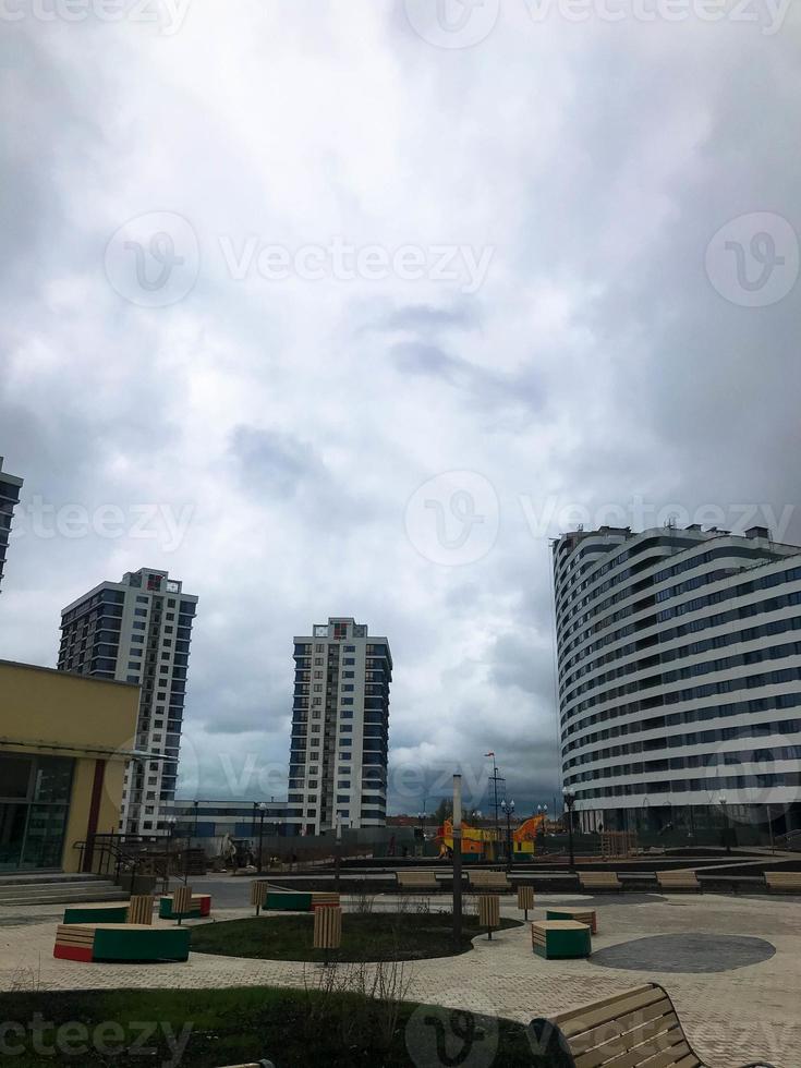 urban landscape with tall glass buildings and blue tenement houses. columns of houses, next to a house of blue and white in the form of a wave. there is a long mall and benches nearby photo