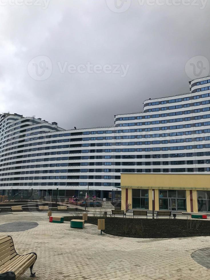 urban landscape with tall glass buildings and blue tenement houses. against the background of the sky there is a bright blue house of an unusual rounded shape. looks like a wave, with white splashes photo