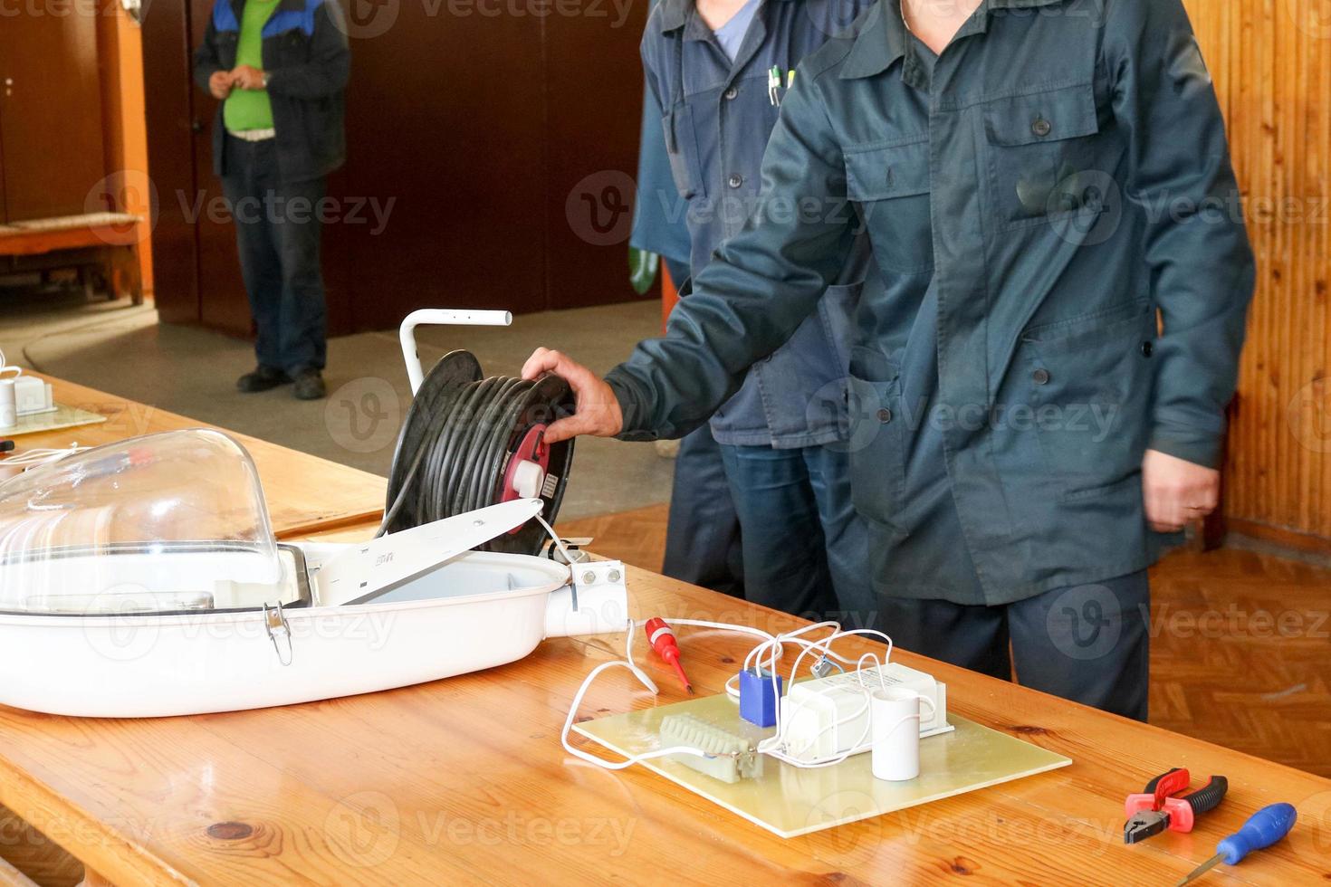 A man working electrician works, collects the electric circuit of a large white street lamp with wires, a relay at an industrial plant factory photo