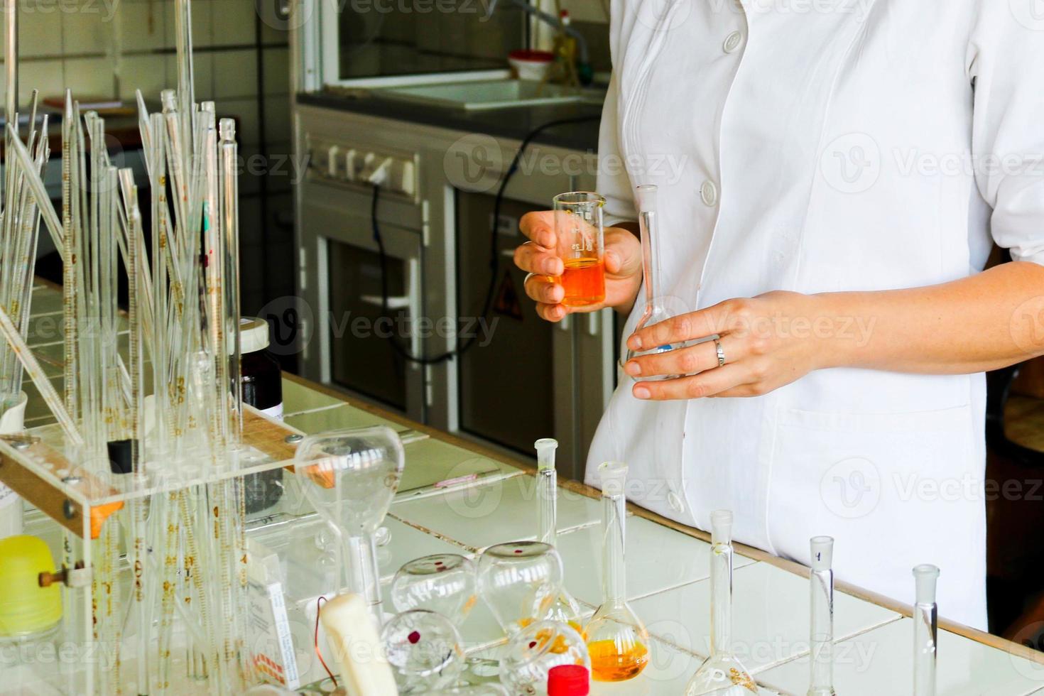 A female laboratory assistant, a doctor, a chemist, works with flasks, test tubes, makes solutions, medicines, mixes the ingredients in the laboratory. Laboratory assistant carries out the research photo