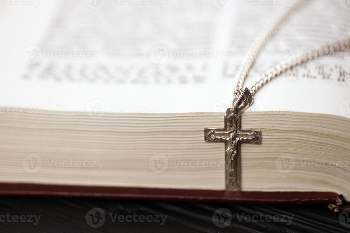 collar de plata con cruz crucifijo en el libro de la santa biblia cristiana sobre una mesa de madera negra. pidiendo bendiciones de dios con el poder de la santidad, que trae suerte foto