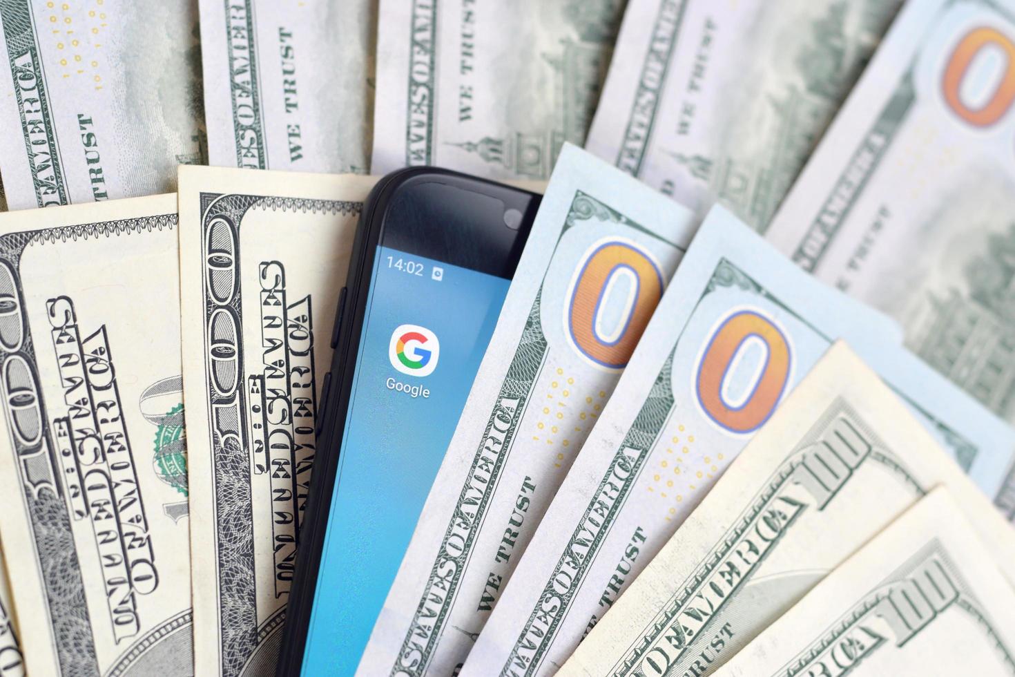 KHARKIV, UKRAINE - MAY 2, 2021 Smartphone screen with Google app and lot of hundred dollar bills. Business and social networking concept photo