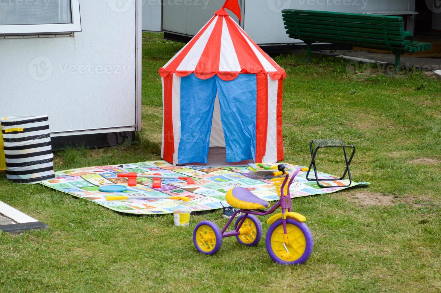 Children's playground in the courtyard of the house on the grass lawn with a tent, a tent toy tricycle photo