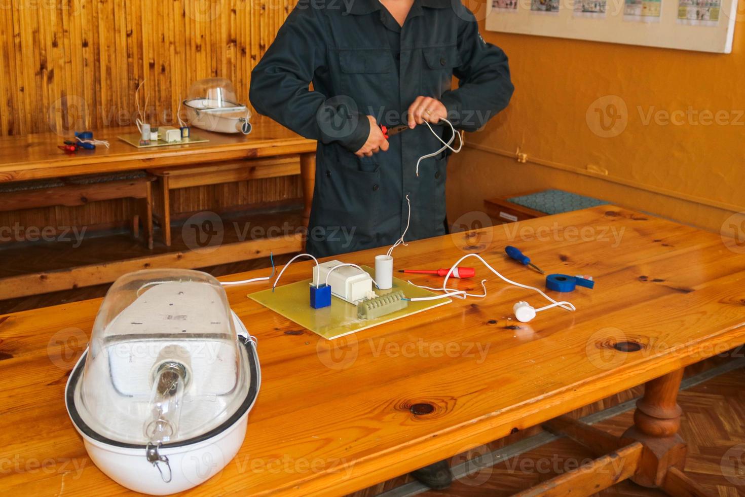 un electricista que trabaja, recoge el circuito eléctrico de una gran farola blanca con cables, un relé en una fábrica de plantas industriales foto