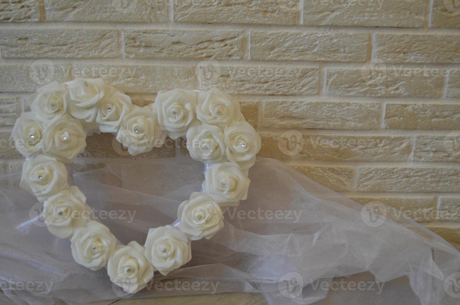 White heart with white roses and rhinestones on a background of beige bricks. photo