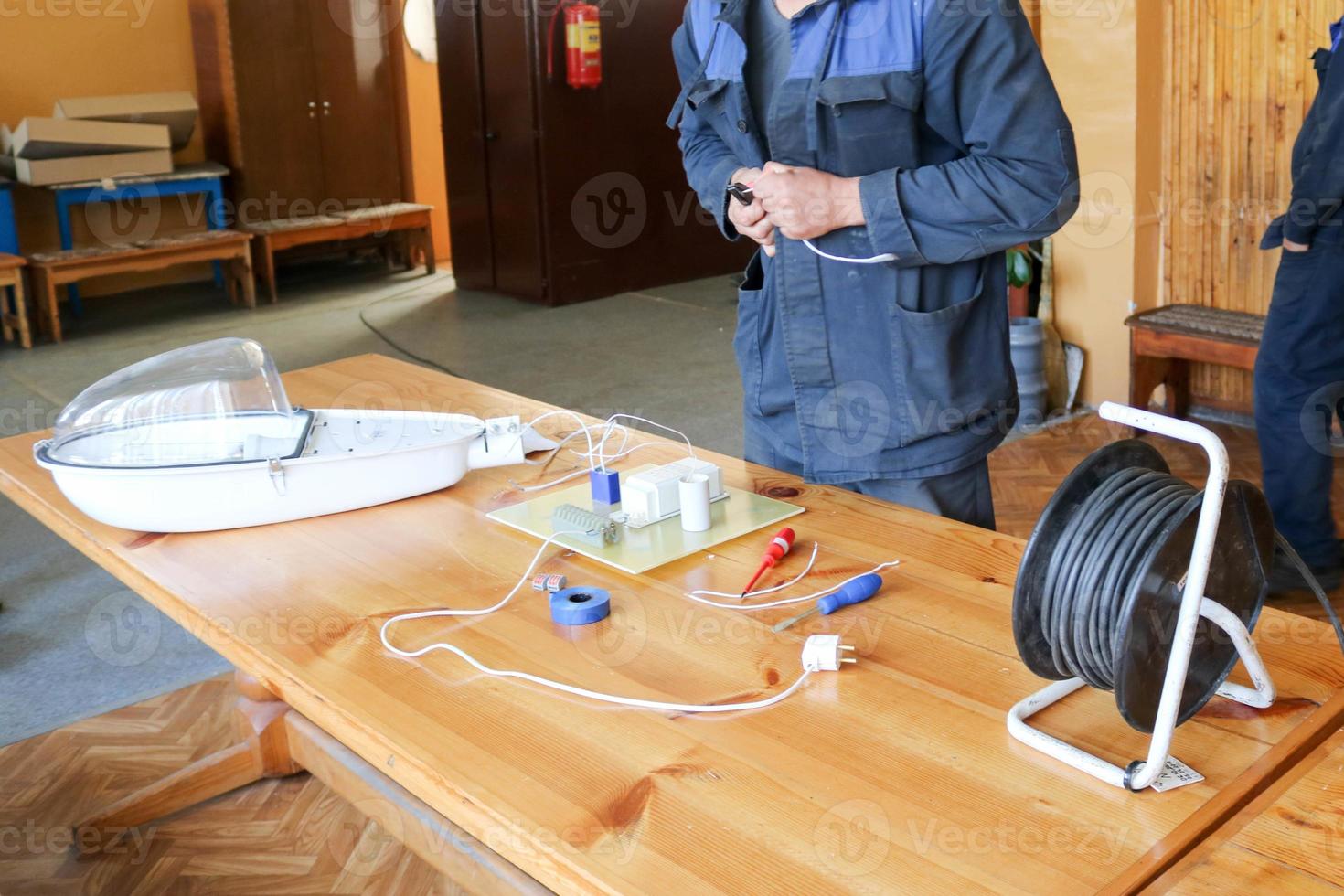 A man working electrician works, collects the electric circuit of a large white street lamp with wires, a relay at an industrial plant factory photo