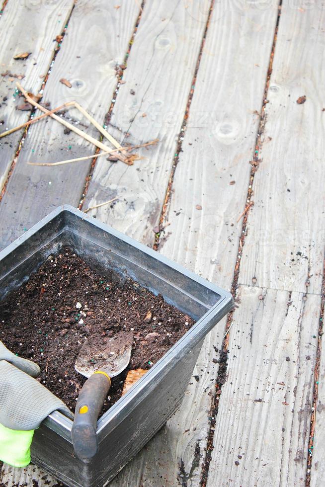 Plant pots with soil prepared for planting and gloves, pickle placed on a wooden balcony scattered with soil. photo