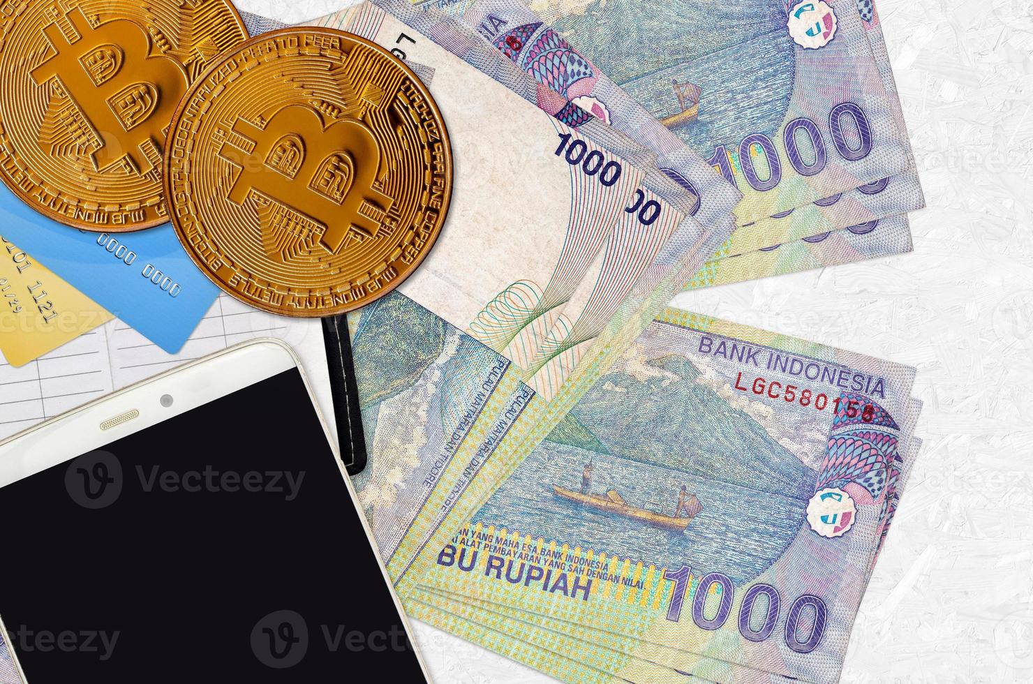 Billetes de 1000 rupias indonesias y bitcoins dorados con smartphone y tarjetas de crédito. concepto de inversión en criptomonedas. criptominería o comercio foto