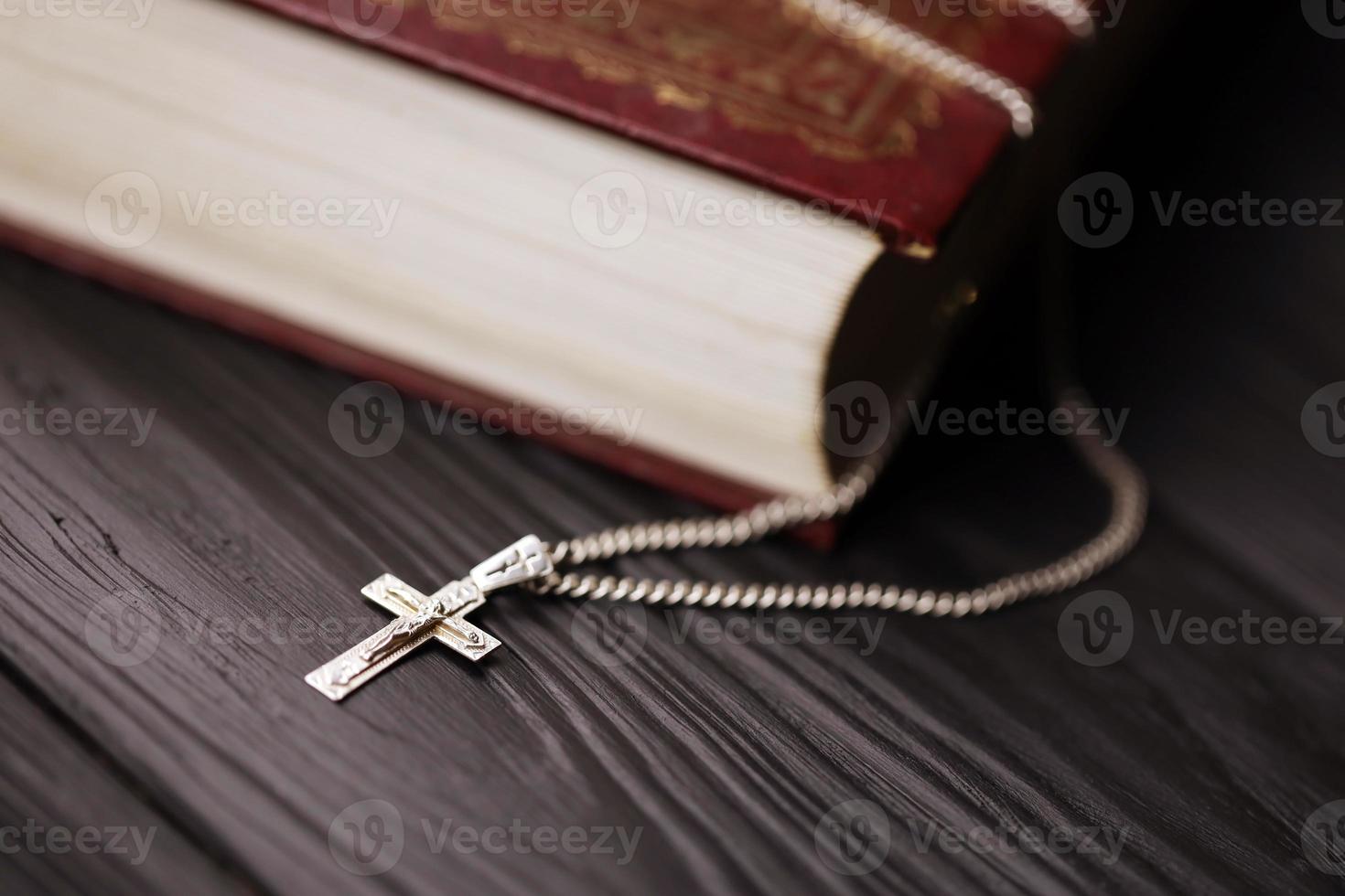 Silver necklace with crucifix cross on christian holy bible book on black wooden table. Asking blessings from God with the power of holiness, which brings luck photo