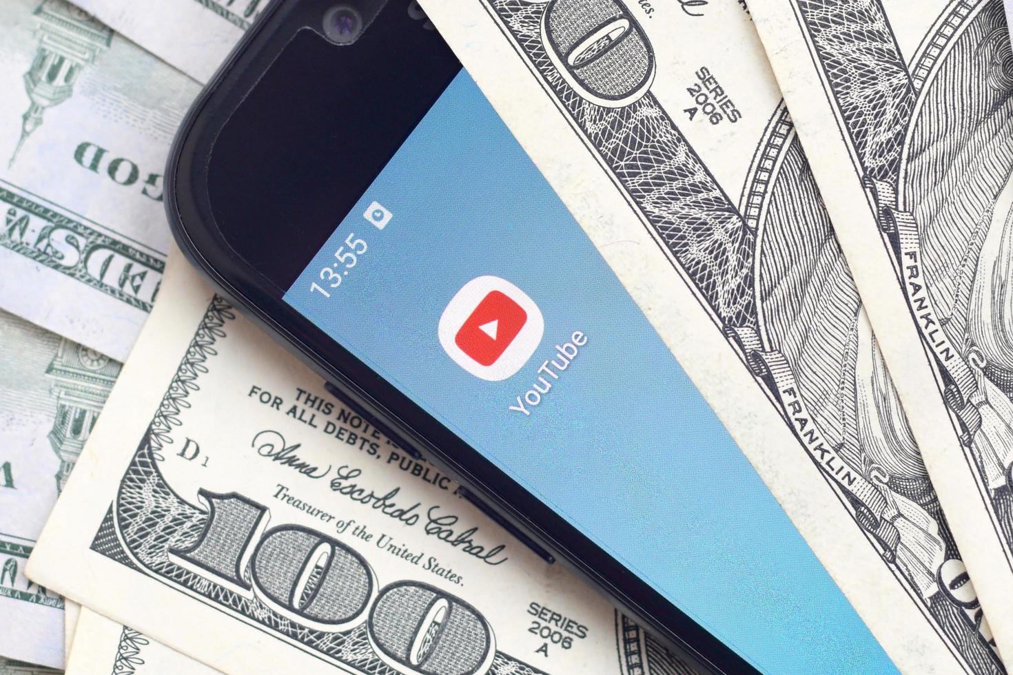 KHARKIV, UKRAINE - MAY 2, 2021 Smartphone screen with Youtube app and lot of hundred dollar bills. Business and social networking concept photo
