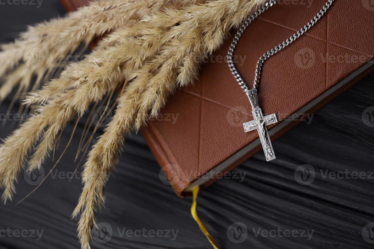 Silver necklace with crucifix cross on christian holy bible book on black wooden table. Asking blessings from God with the power of holiness photo