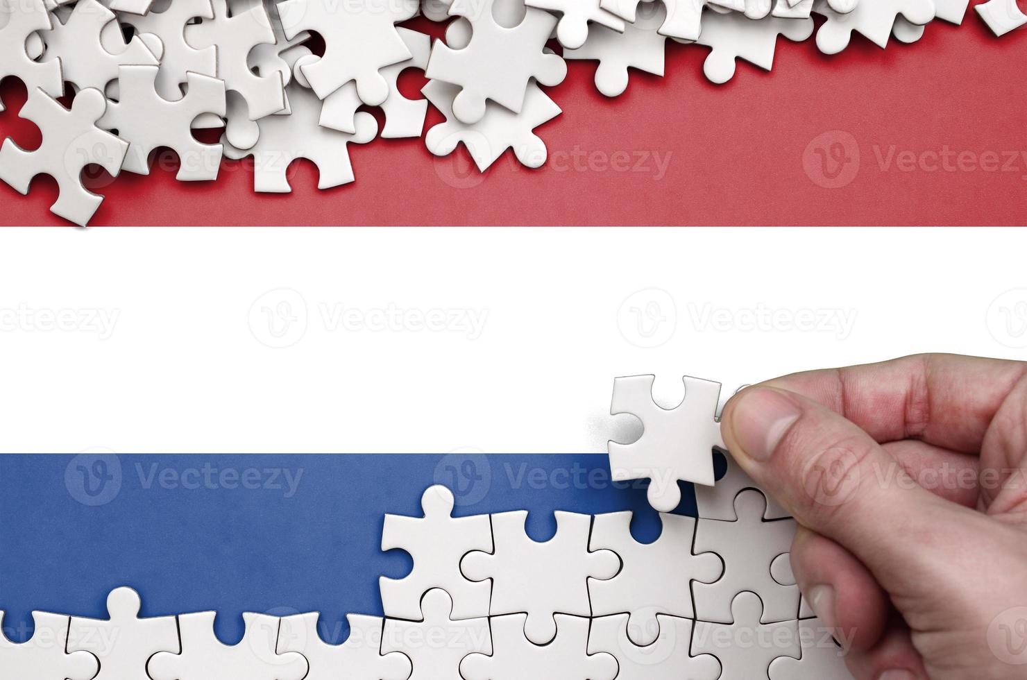 Netherlands flag  is depicted on a table on which the human hand folds a puzzle of white color photo