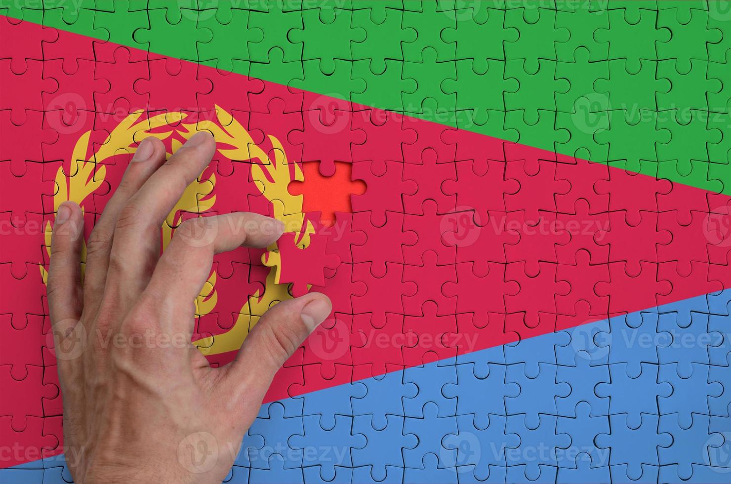 Eritrea flag  is depicted on a puzzle, which the man's hand completes to fold photo