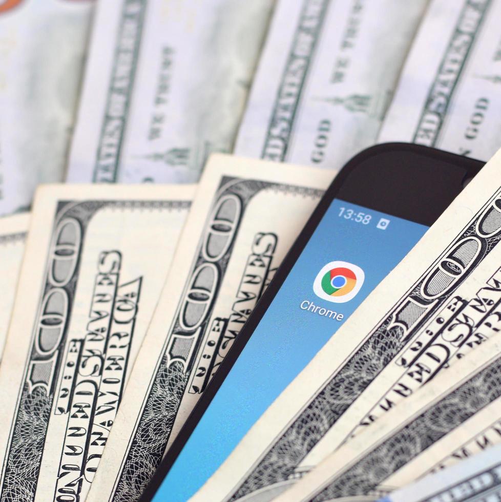 KHARKIV, UKRAINE - MAY 2, 2021 Smartphone screen with Google chrome app and lot of hundred dollar bills. Business and social networking concept photo