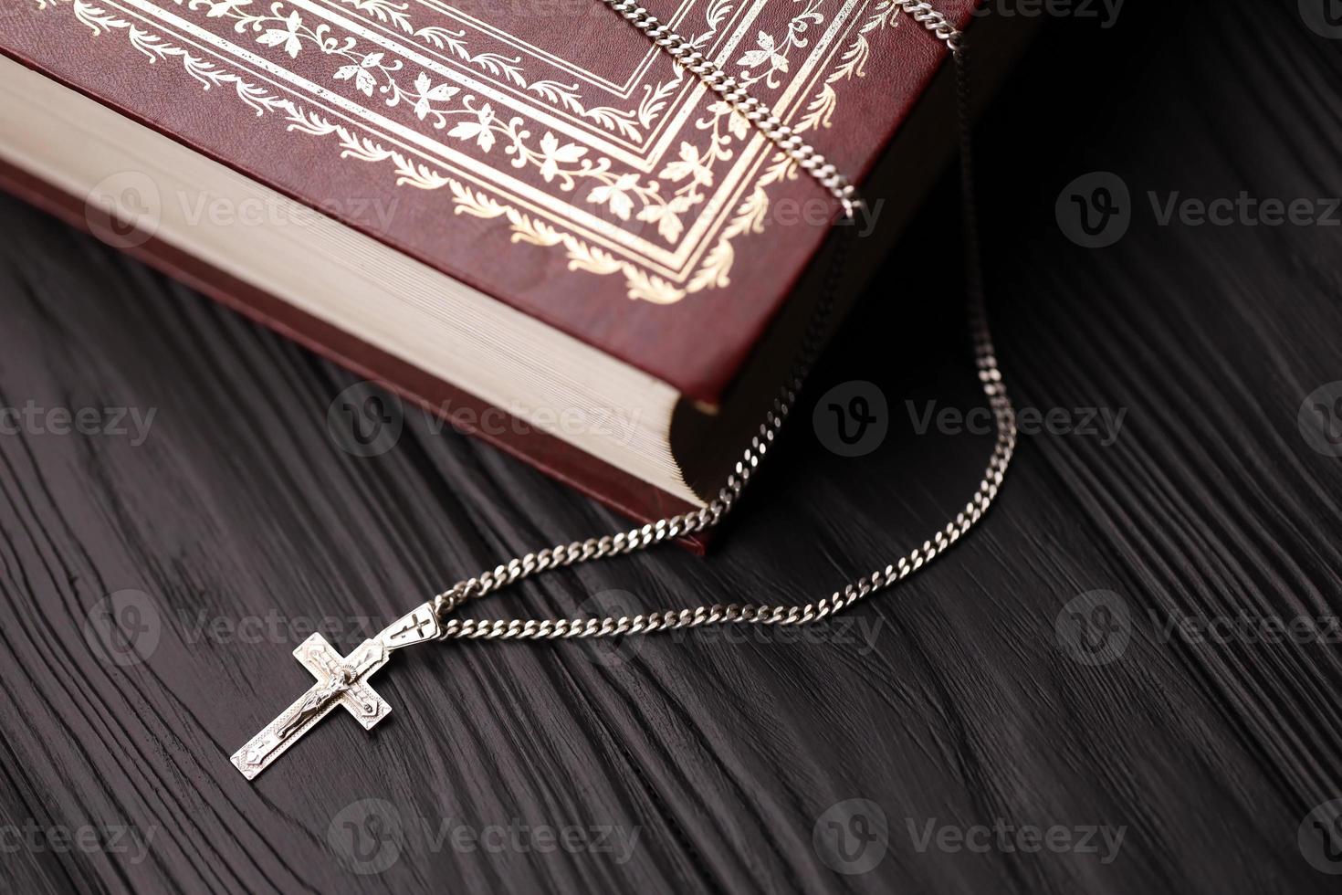 Silver necklace with crucifix cross on christian holy bible book on black wooden table. Asking blessings from God with the power of holiness, which brings luck photo