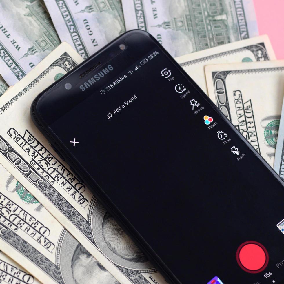 KHARKIV, UKRAINE - MAY 2, 2021 Smartphone screen with Tiktok app and lot of hundred dollar bills. Business and social networking concept photo