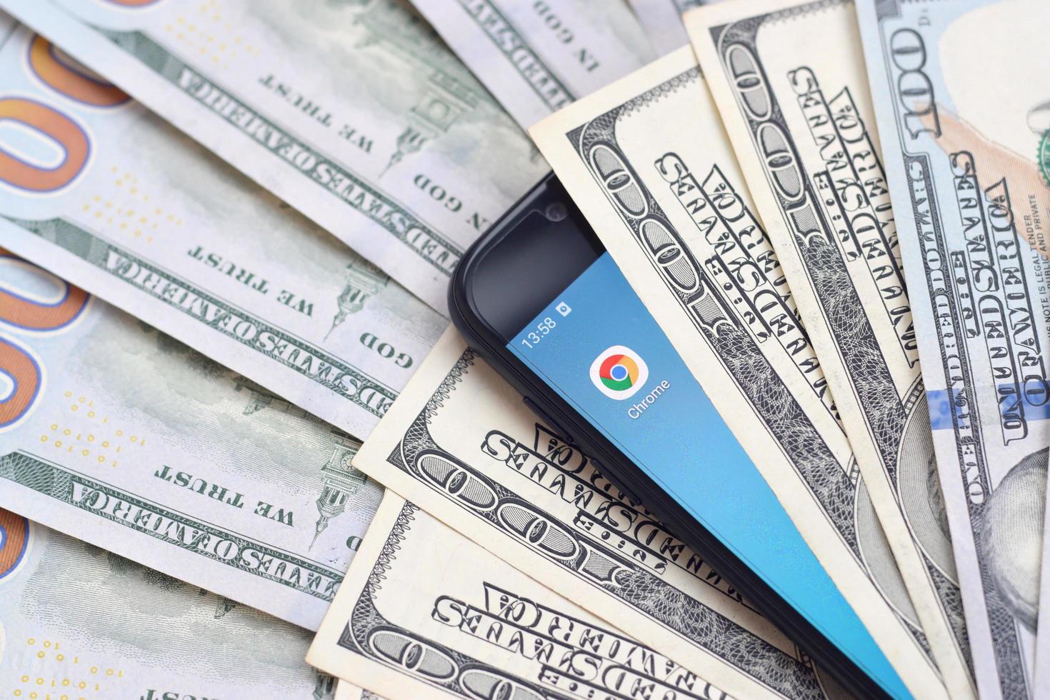 KHARKIV, UKRAINE - MAY 2, 2021 Smartphone screen with Google chrome app and lot of hundred dollar bills. Business and social networking concept photo