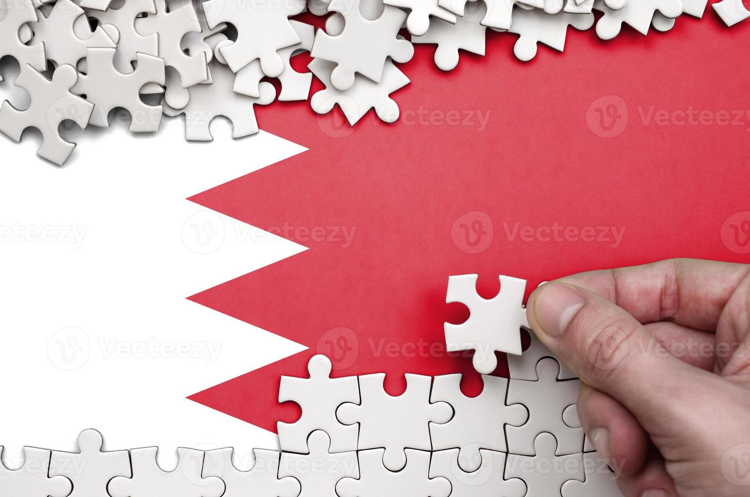 Bahrain flag  is depicted on a table on which the human hand folds a puzzle of white color photo