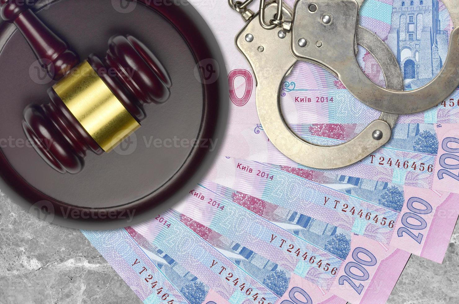 200 Ukrainian hryvnias bills and judge hammer with police handcuffs on court desk. Concept of judicial trial or bribery. Tax avoidance photo