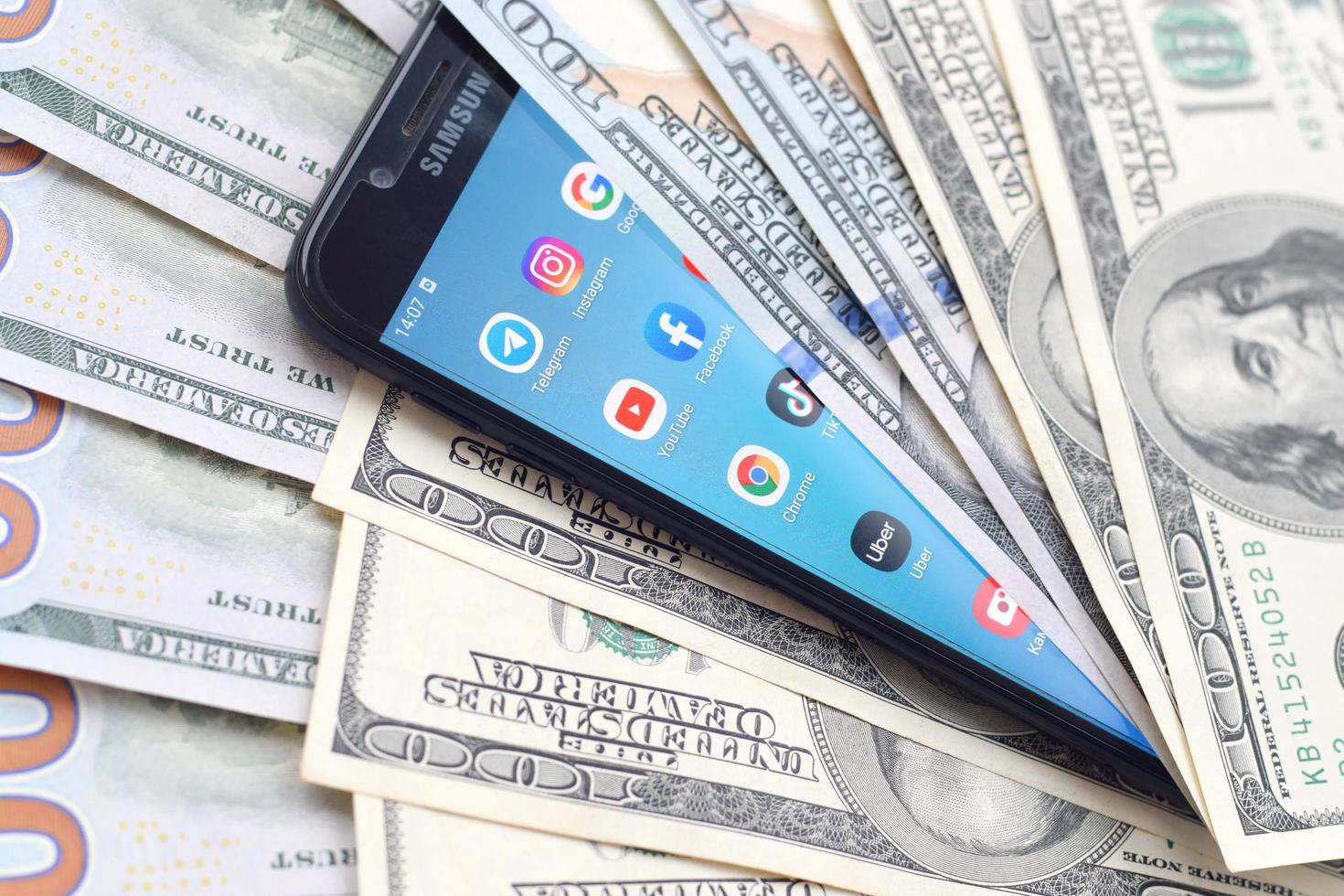 KHARKIV, UKRAINE - MAY 2, 2021 Smartphone screen with many popular apps and lot of hundred dollar bills. Business and social networking concept photo