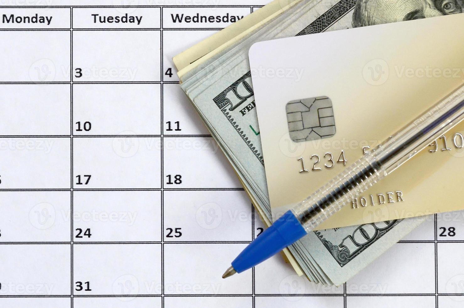 Pen and credit card on many hundred US dollar bills on calendar page close up photo