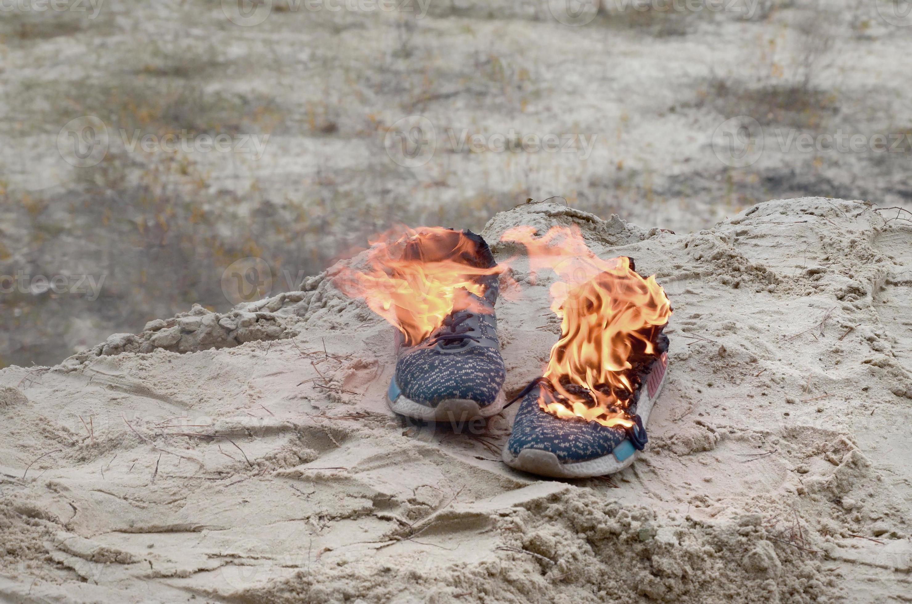 Burning sports sneakers or gym shoes on fire stand on sandy beach coast