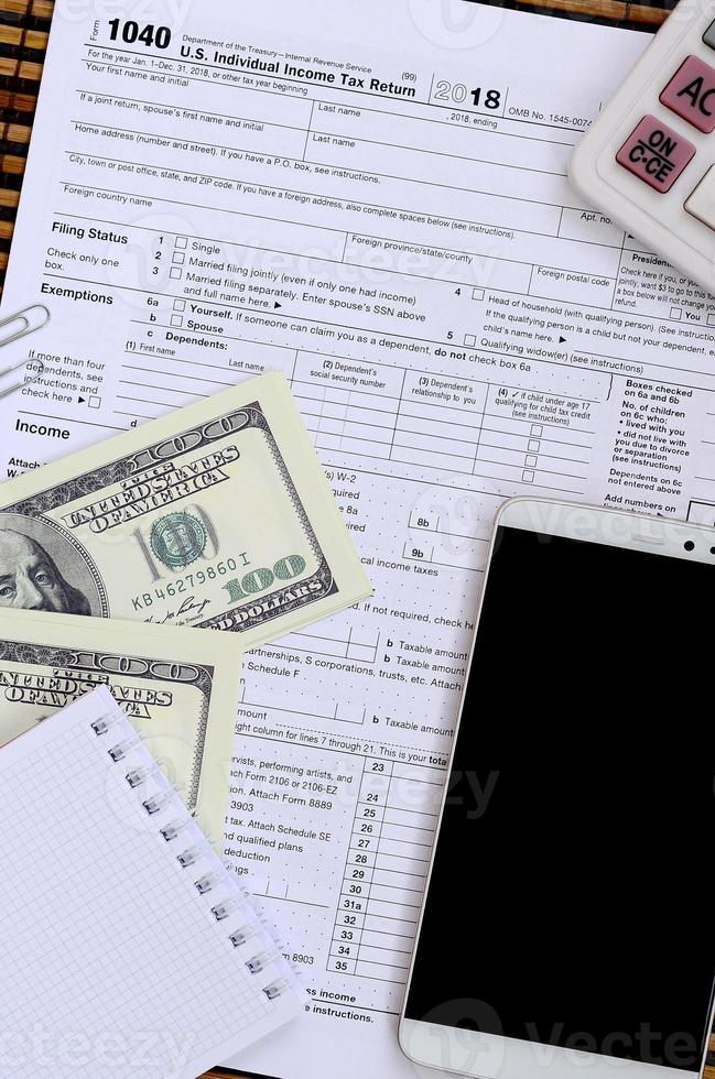 Composition of items lying on the 1040 tax form. Dollar bills, calculator, smartphone, paper clip and notepad. The time to pay taxes photo
