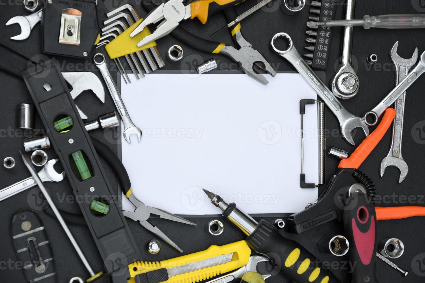 Handyman tool kit on black wooden table with copy space in blank paper tablet. Many wrenches and screwdrivers, pilers and other tools for any types of repair or construction works photo