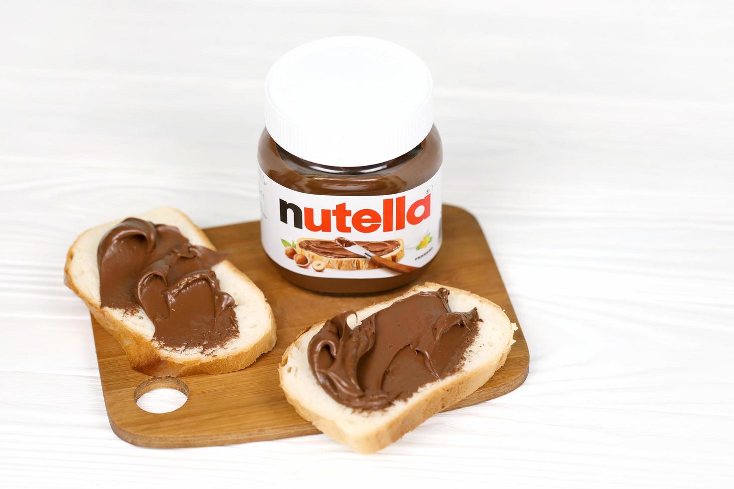 KHARKOV, UKRAINE - DECEMBER 27, 2020 Nutella glass can and spread on freshly baked bread. Nutella is manufactured by Italian company Ferrero first introduced in 1964 photo