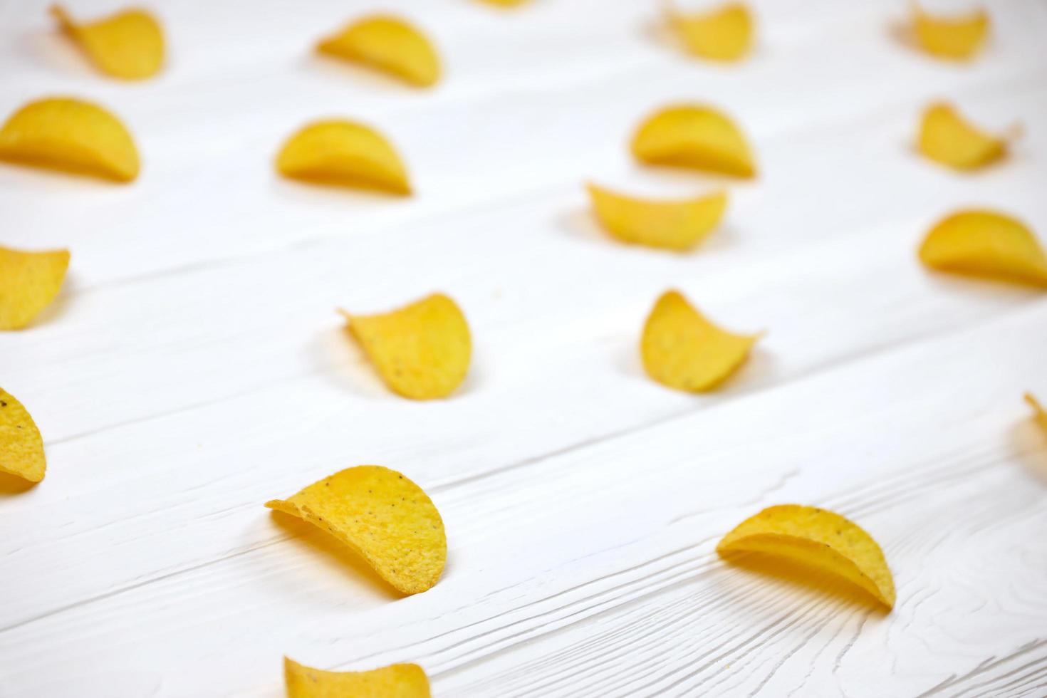KHARKIV, UKRAINE - MAY 02, 2021 Many orange Pringles potato snack chips on white wooden table. Pringles is a brand of potato snack chips owned by Kellogg Company photo