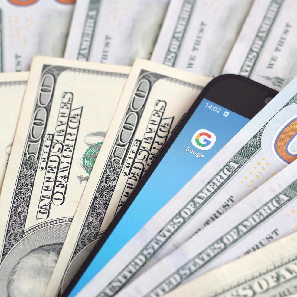 KHARKIV, UKRAINE - MAY 2, 2021 Smartphone screen with Google app and lot of hundred dollar bills. Business and social networking concept photo