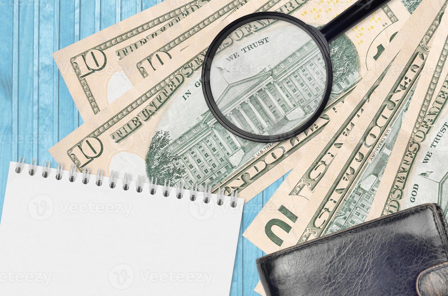 10 US dollars bills and magnifying glass with black purse and notepad. Concept of counterfeit money. Search for differences in details on money bills to detect fake photo