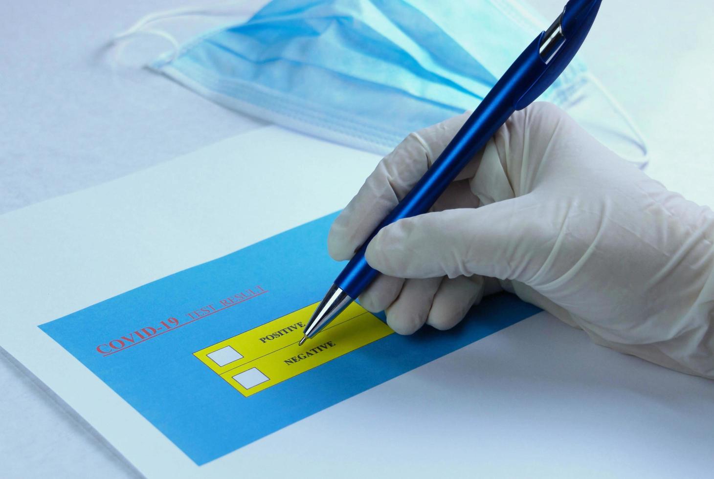 hand wearing medical gloves holding pen to check on Covid-19 test result photo