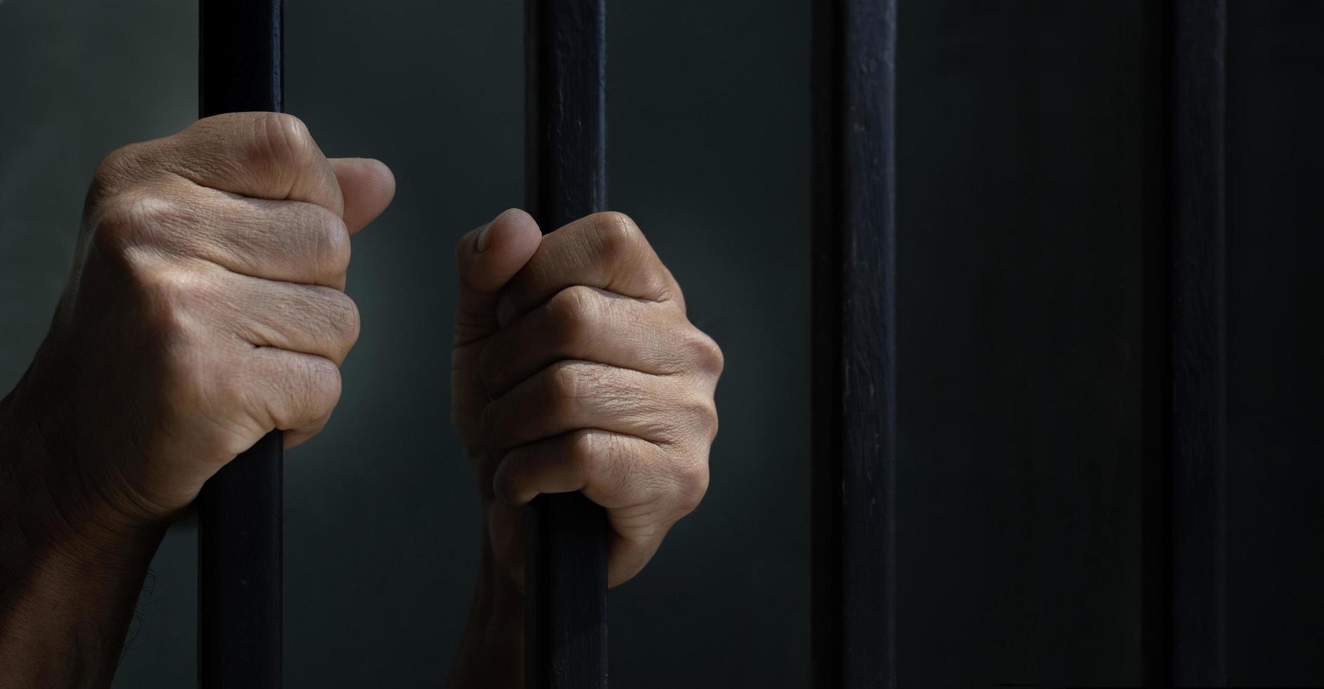 Hand of convicted prisoner behind the cell bar inside jail for incarceration, criminal and limited freedom concept photo