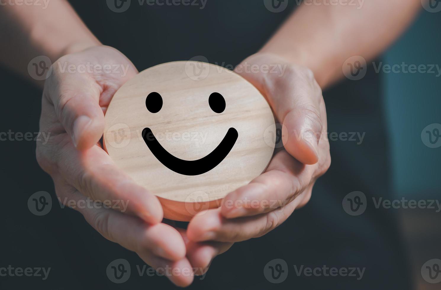 Hands holding wooden happy smile face, good feedback rating and positive customer review,experience, satisfaction survey,mental health assessment,child feeling good,world mental health day. photo