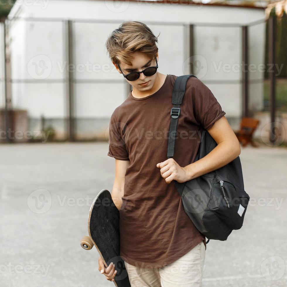 Young handsome guy in stylish clothing walking with a skateboard. photo