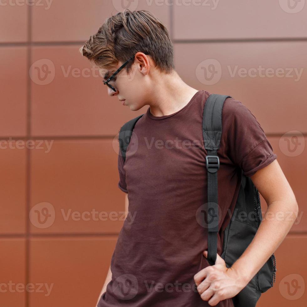 joven apuesto con una camiseta y gafas de sol, sosteniendo una mochila. foto