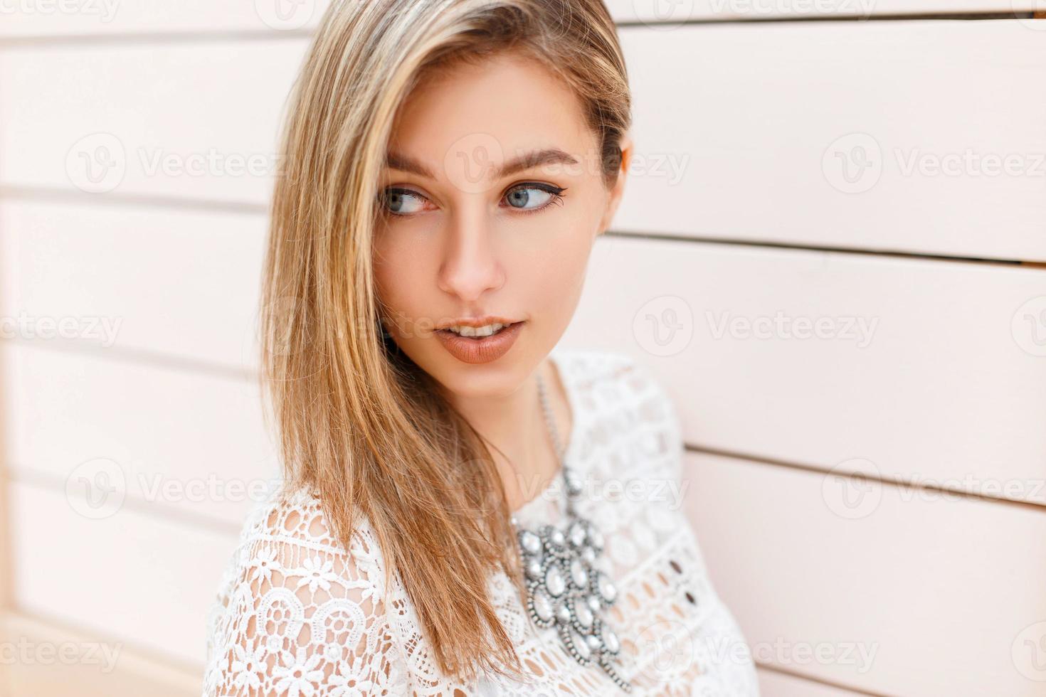 retrato de primer plano de una hermosa mujer con una elegante blusa de encaje blanco vintage mira hacia un lado sobre un fondo de una pared de madera foto