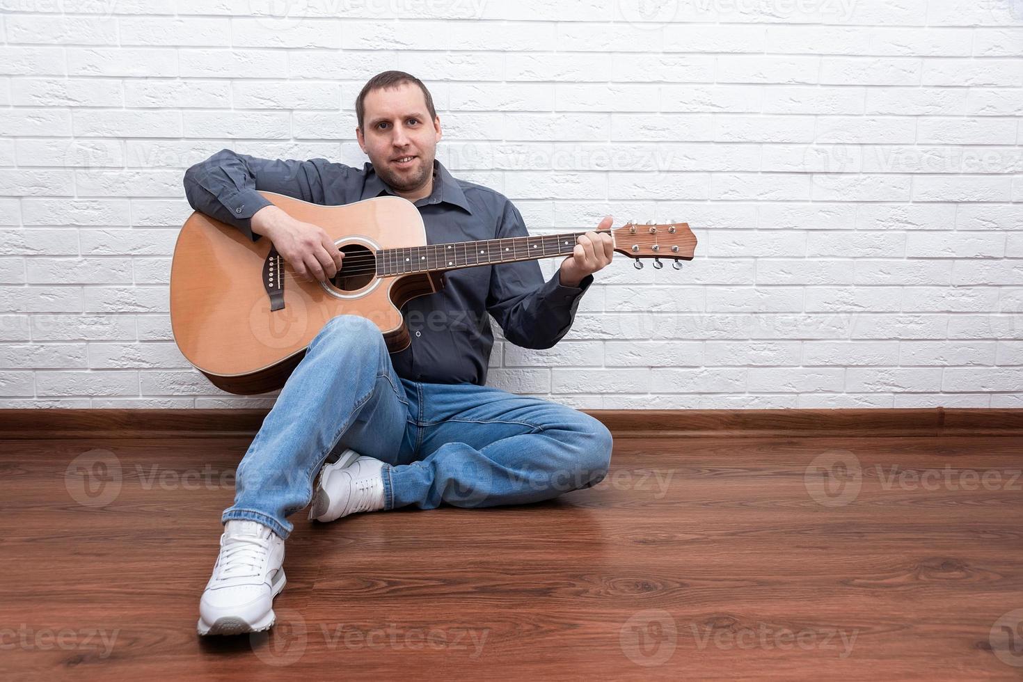 Handsome man with guitar against brick wall photo