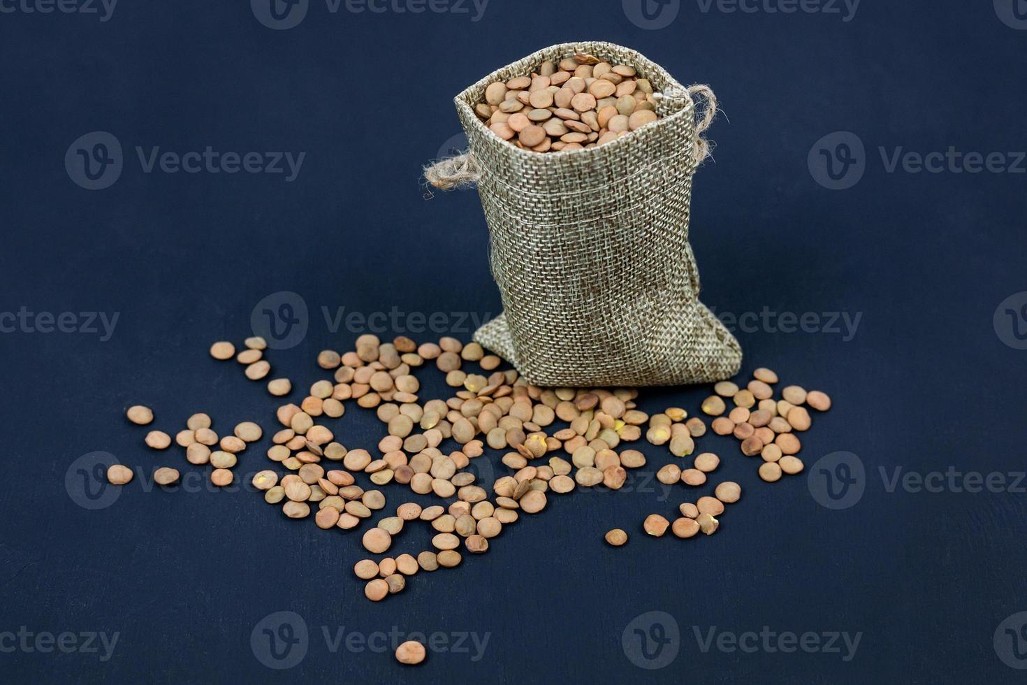 brown dried lentils in a burlap bag on black background photo