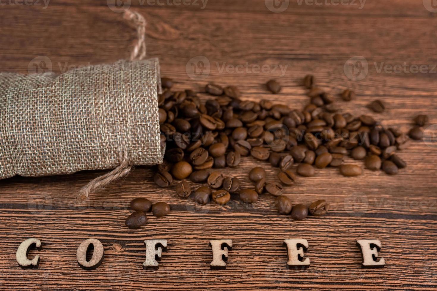 Black coffee foil packaging bag on wooden table top view. Spilled beans flat lay concept. Room for text. photo