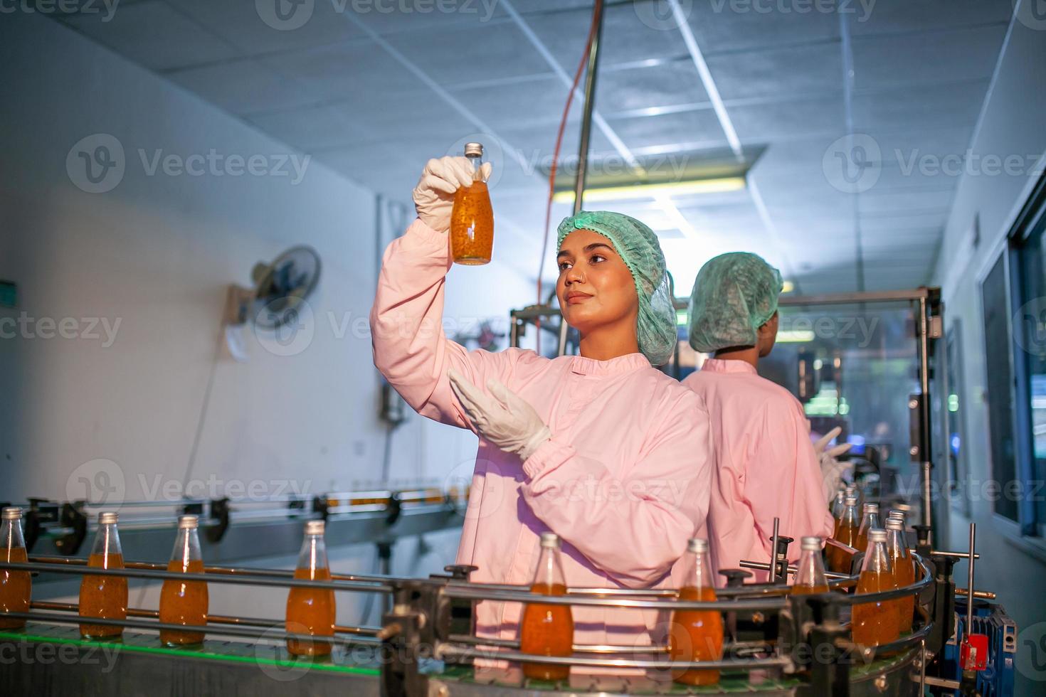 Asian woman worker is checking product bottles of fruit juice on the production line in the beverage factory. Manufacturer checks quality of food industry. photo