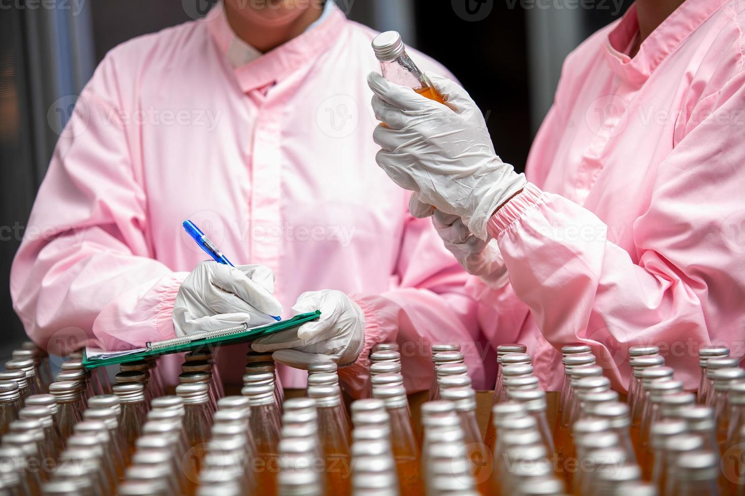 Asian woman worker with clipboard is checking product bottles of fruit juice on the production line in the beverage factory. Manufacturer checks quality of food industry. photo